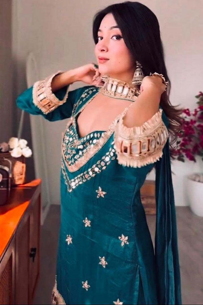 Woman in a traditional teal and gold outfit indoors